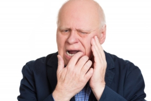 Man in pain pointing to a sore spot under his denture needing an adjustment