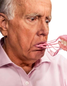 Man pulling out his dentures from his mouth with many strands of denture adhesive goop following and still attached to his mouth