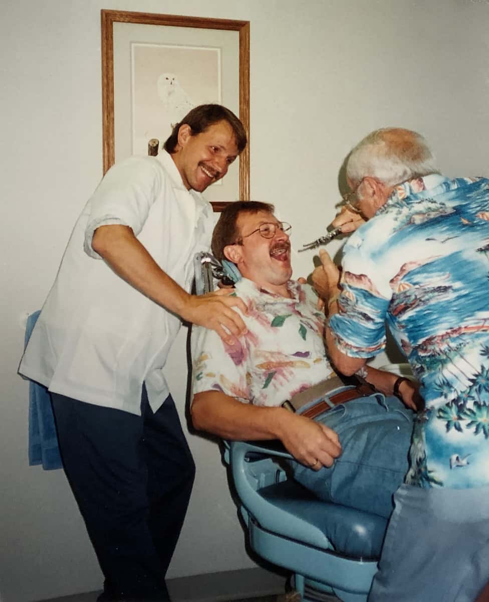 Denturist Joe Schankula hamming it up with a smiling Tim and Tim's visiting cousin in the dental chair with mouth wide open ready to receive an scary instrument into his mouth by Joe