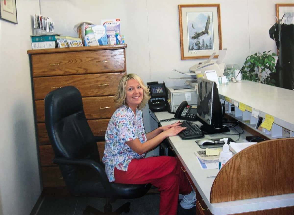 Receptionist and lab assistant, Linda, sitting at the front desk computer and smiling at the camera