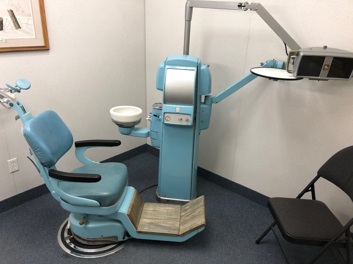 The dental chair, dental machinery holding the spit bowl and controlling water and lights and holding the instrument tray and light on swivel arms, with a soft folding chair for anyone a patient wishes to have in with them during their procedures