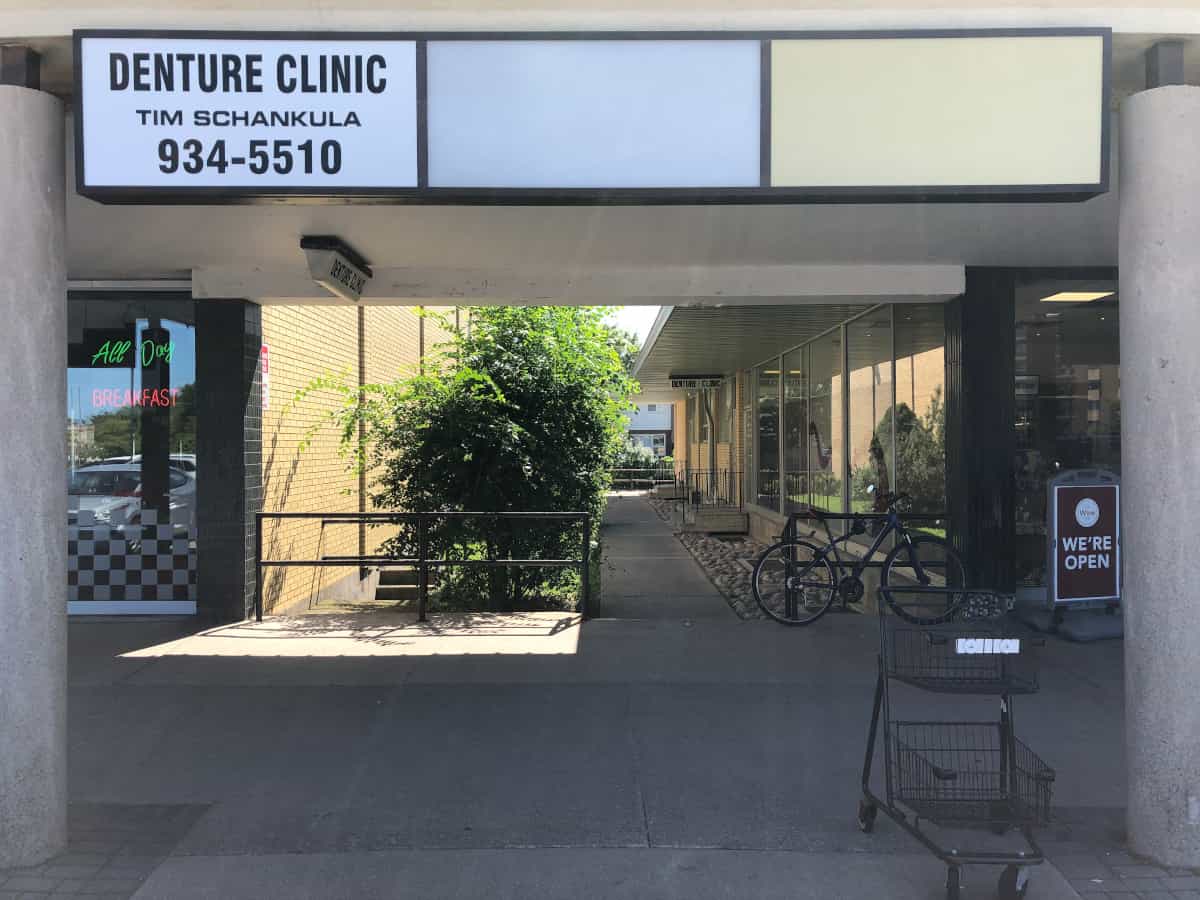 Entrance to the garden alleyway to Grantham Denture Clinic, with Tim Schankula Denture Clinic sign with phone number 905-934-5510, closeup, with the hanging "Denture Clinic" sign on the overhang half way down the garden path in the distance marking the entrance to the clinic