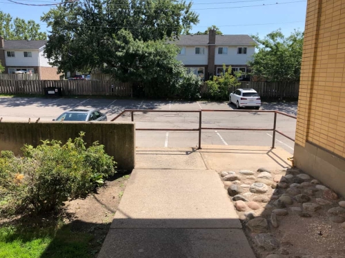 63-The end of the garden alleyway at the rear of the plaza, showing some bushes, sidewalk and staircase railing going down to the rear parking lot showing a couple of parked cars and backyards of houses