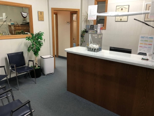 27-Wide shot of our reception desk, some waiting room chairs, some plants, a floor air purifier, large one-way mirror/glass window into the lab and a doorway leading to the rest of the clinic