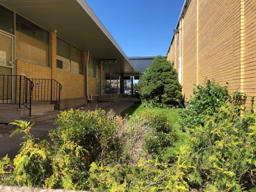 A patient's point of view if they were near the top of the stone staircase at the rear of the plaza, looking down the length of the garden alleyway towards the front parking lot, seeing the Denture Clinic sign above our entrance