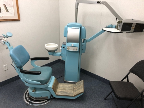 40-The dental chair, dental machinery holding the spit bowl and controlling water and lights and holding the instrument tray and light on swivel arms, with a soft folding chair for anyone a patient wishes to have in with them during their procedures