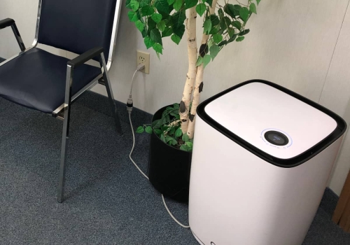 Closeup of the large floor air purifier, next to an artificial plant and chair
