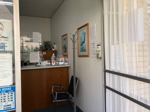A patient's point of view crossing our threshold into our reception area, showing a coat tree, a chair, and pamphlets on our reception desk countertop, with a wall-mounted hand-sanitizer dispenser just inside the door