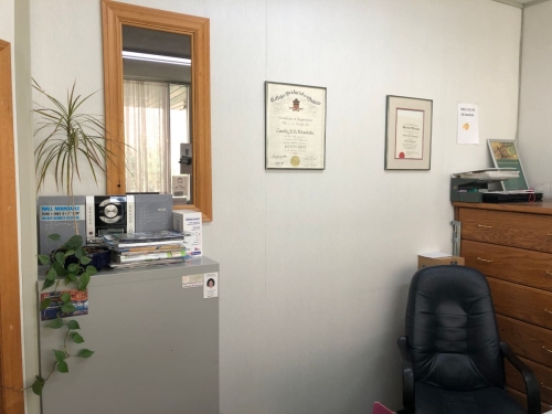 33-The wall behind the reception desk showing a wood-framed mirror and diplomas, a metal filing cabinet on the left with a plant, radio and magazines on top, a beautiful wooden cabinet on the right and the receptionist's soft leather computer chair