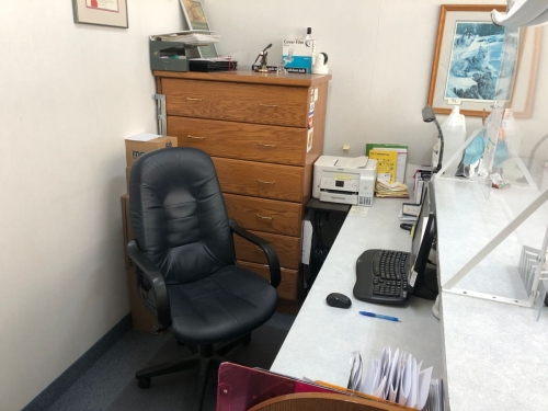 34-The receptionist's working area, with a soft leather computer chair, computer screen, keyboard and mouse, printer, beautiful wooden cabinet in the background and patient files and clipboards in the foreground